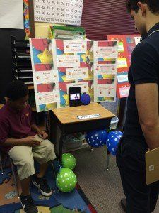 A boy is sitting at a desk in a classroom with balloons around it.