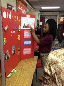 A girl is standing in front of a red board that says old vs new gum