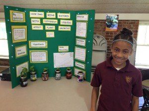 A young girl is standing in front of a science project.