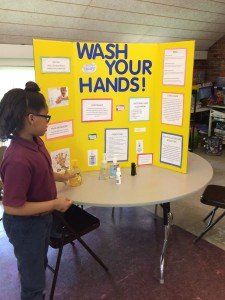 A girl is standing in front of a sign that says wash your hands