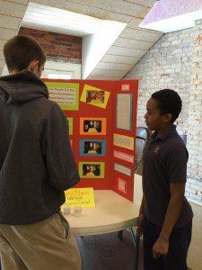 Two boys are standing in front of a red board with pictures on it
