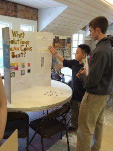 A boy is pointing at a poster that says `` what solutions mean coins best ''.