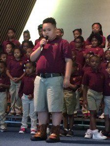 A boy singing into a microphone in front of a choir