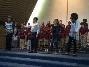 A group of children are standing on a stage in front of a choir.