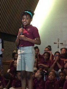 A girl is holding a microphone in front of a crowd of children