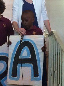 A boy is holding a sign with the letter a painted on it