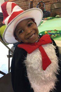 A little boy is wearing a cat in the hat costume and smiling.