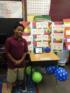 A young boy is standing in front of a desk decorated with balloons.