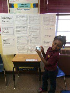 A young girl is taking a picture of a poster in a classroom.