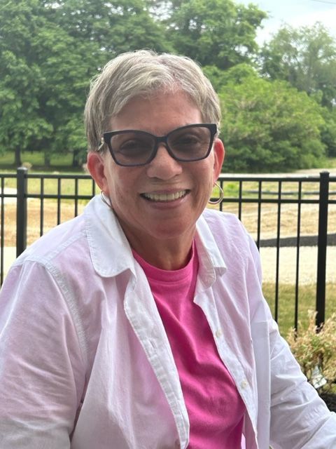 A woman wearing sunglasses and a pink shirt is smiling for the camera.