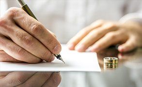 A man writing on a document, with his wedding ring on the table