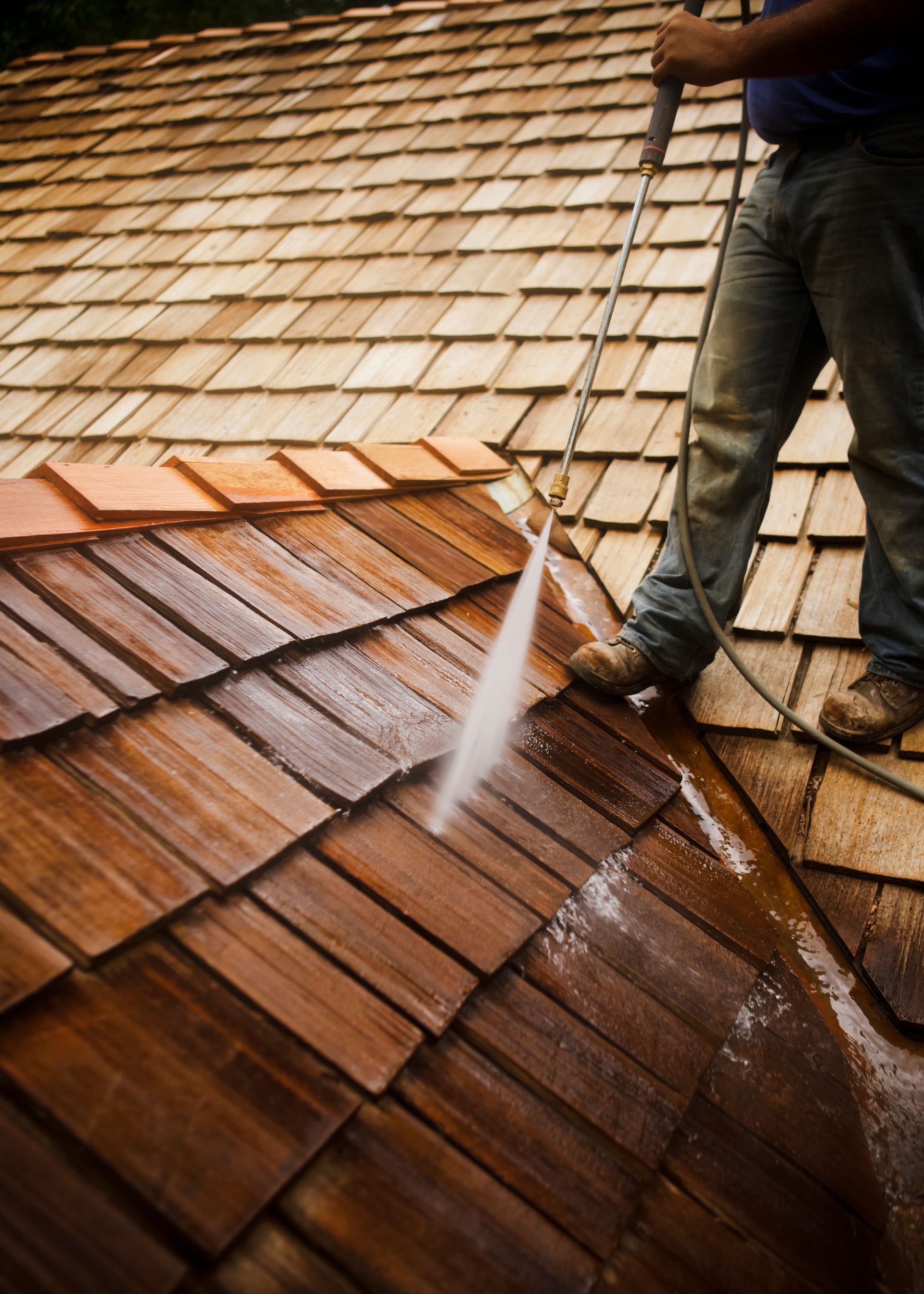 A man is cleaning a wooden roof with a high pressure washer