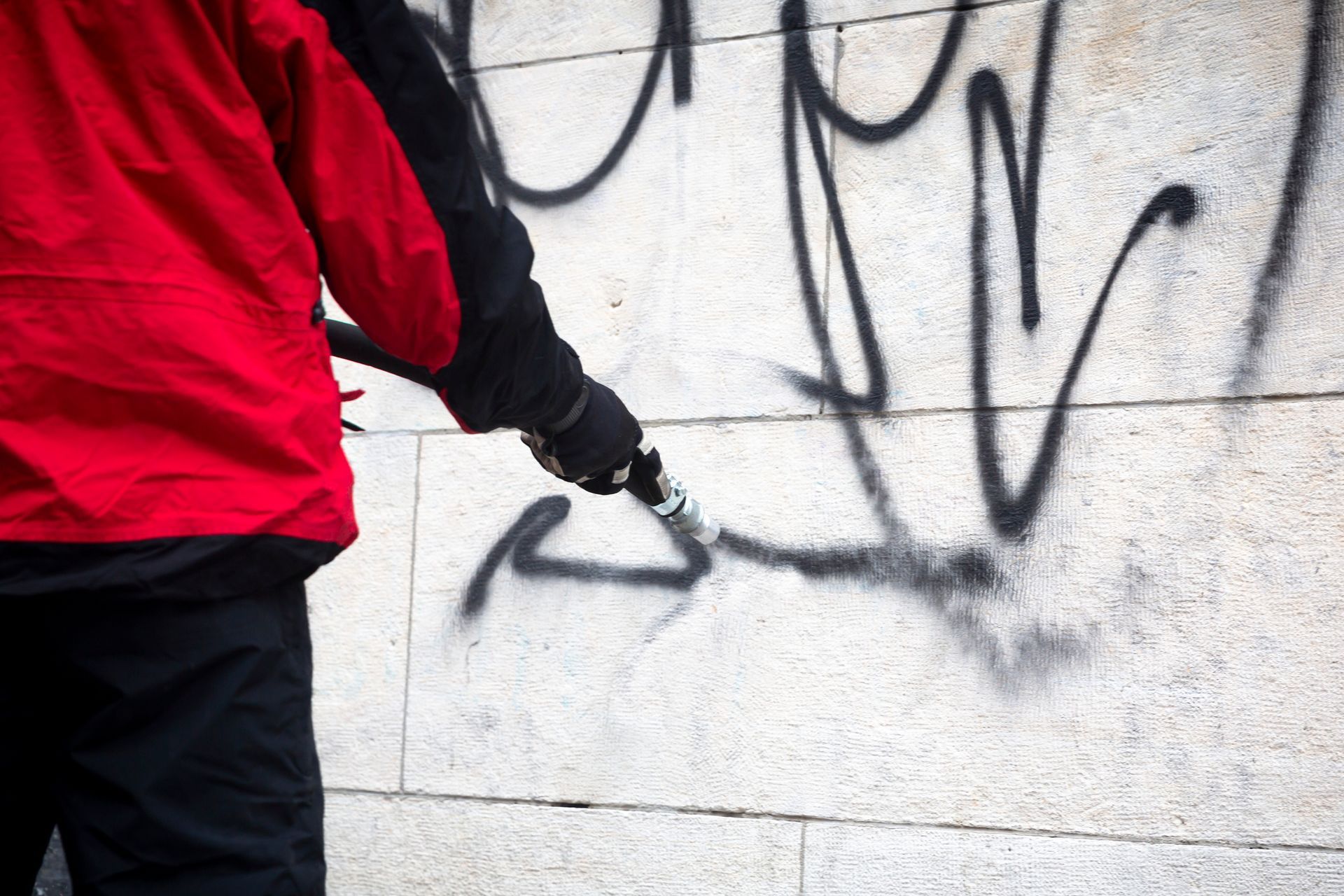 A person in a red jacket is spray painting graffiti on a wall.