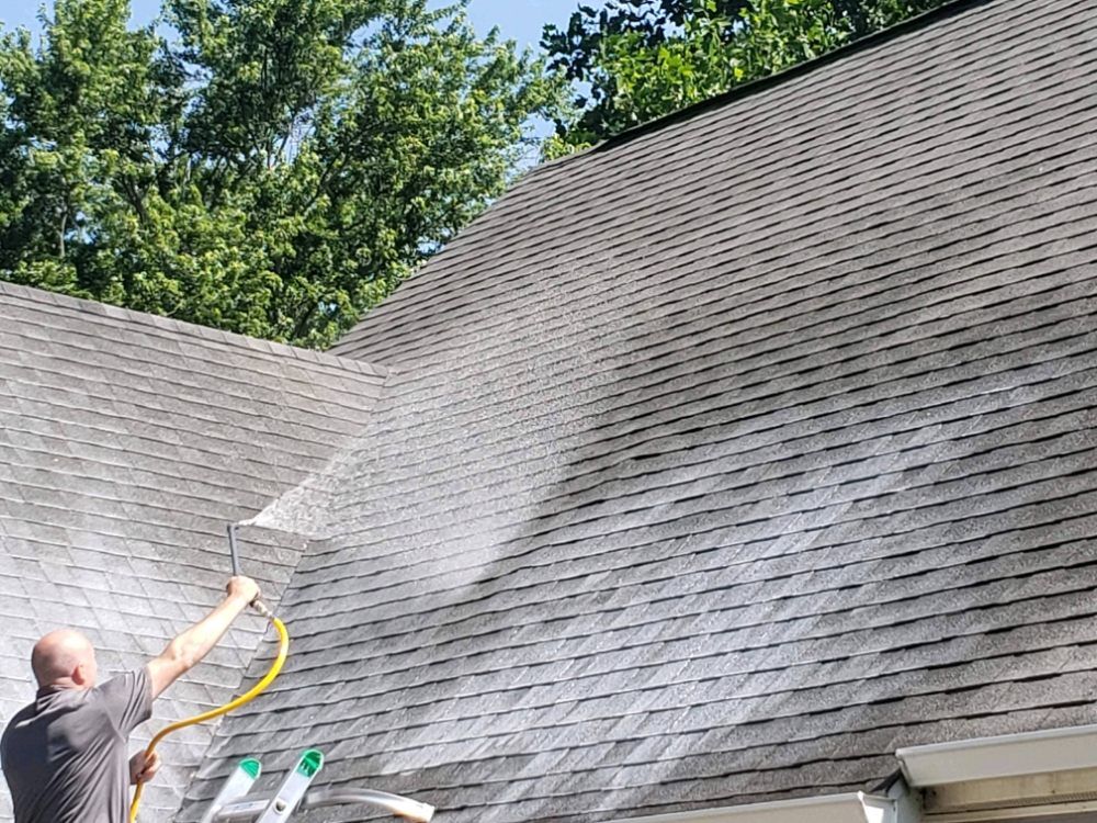 A man is cleaning the roof of a house with a hose.