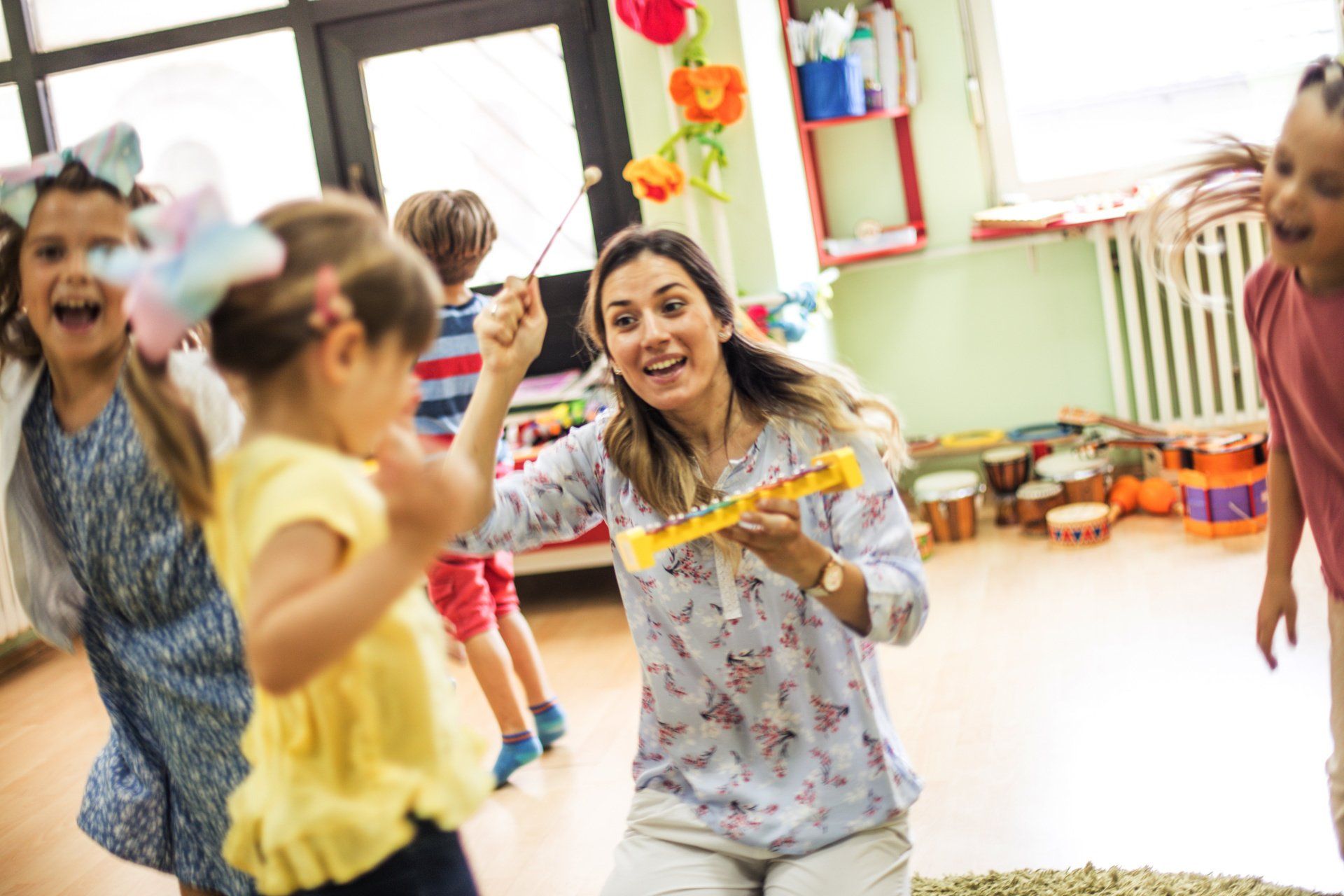 A woman is playing a musical instrument with a group of children in a classroom.
