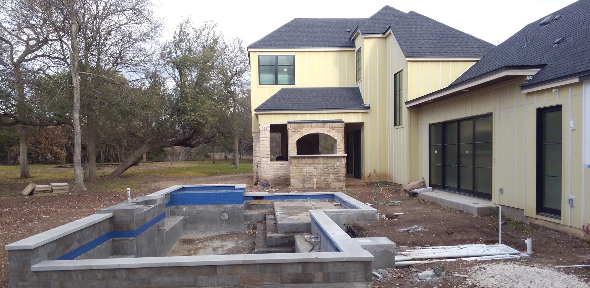 A house exterior with an unfinished pool. The home is yellow with dark roof tiles.