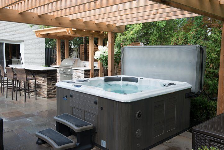 Hot tub under a pergola on a patio with outdoor kitchen.