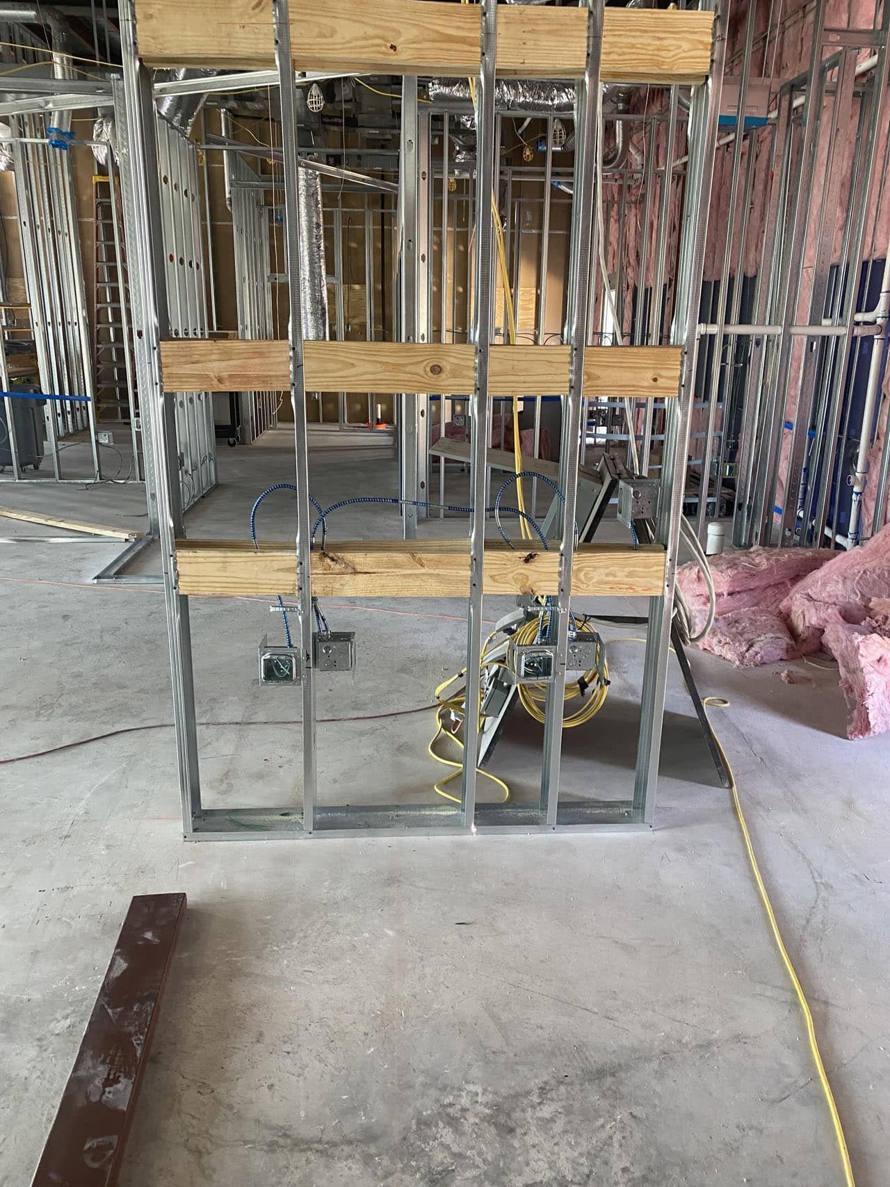 Metal framing for a wall with wooden supports and electrical wiring in a construction site.