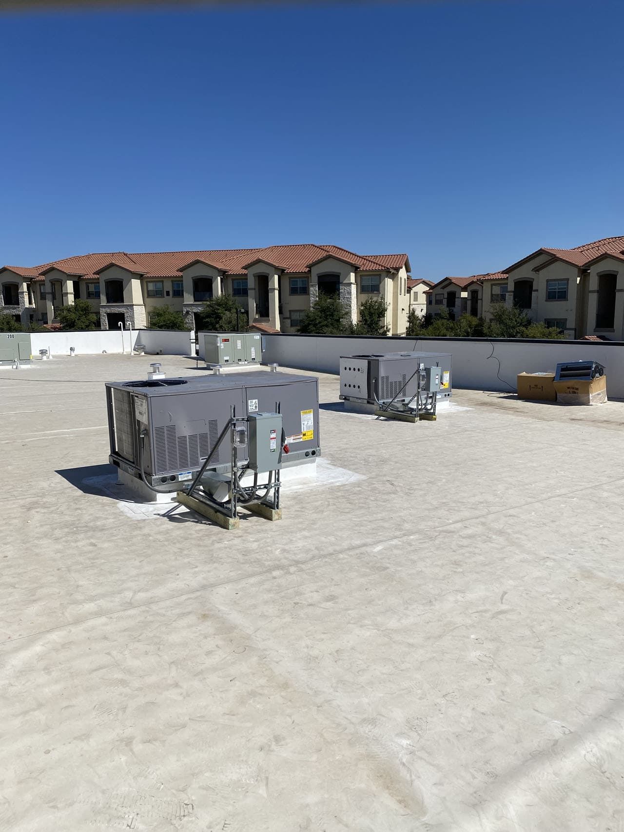 Rooftop with HVAC units; apartment buildings in the background under a blue sky.
