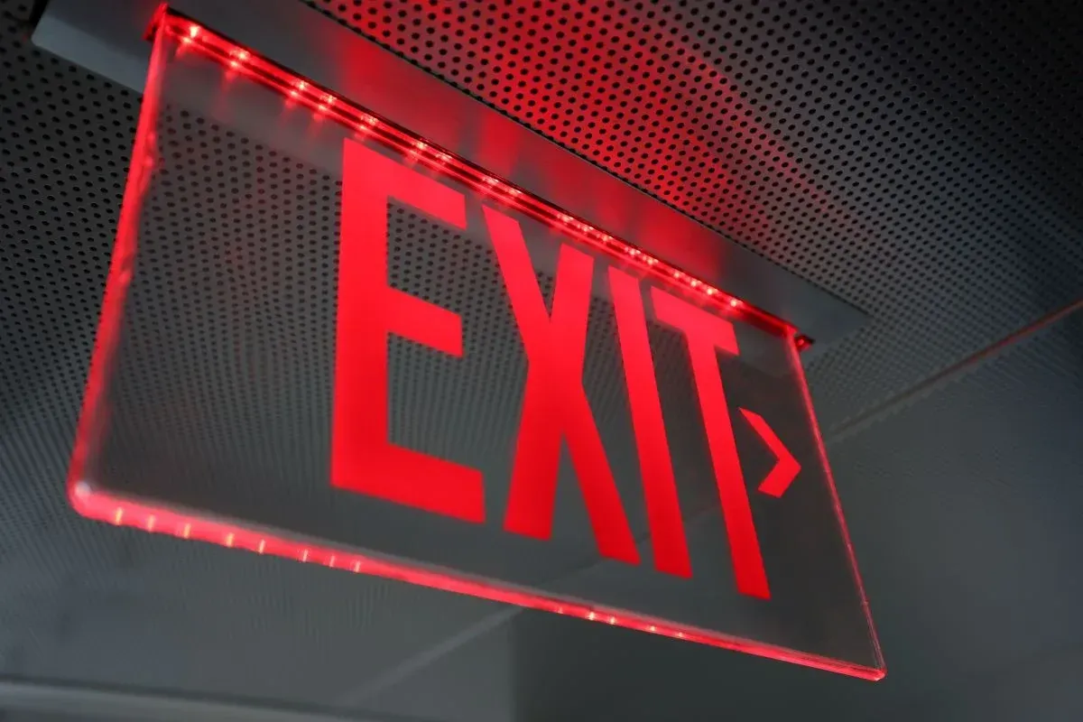 Red lit exit sign with an arrow, mounted on a ceiling.