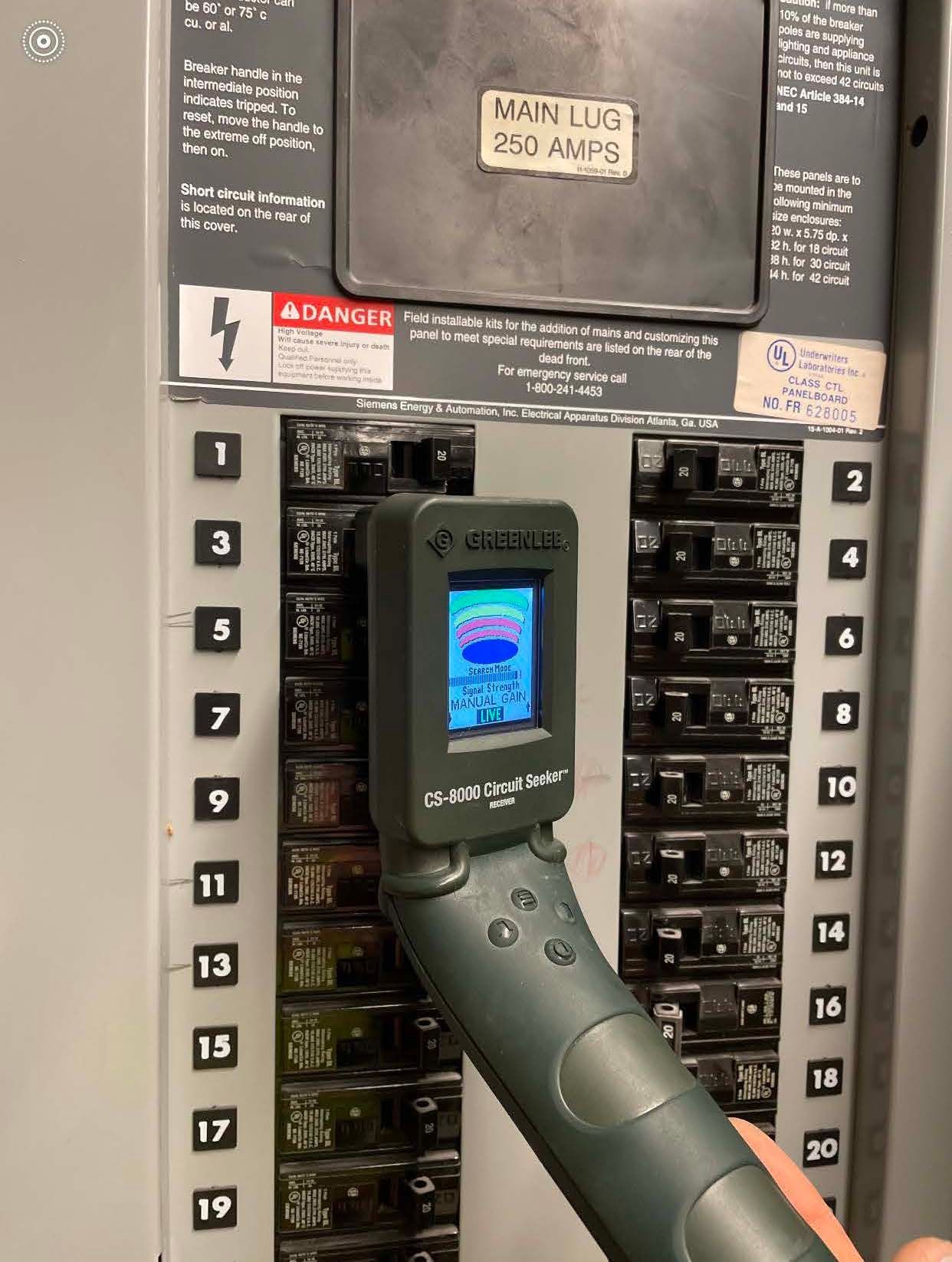 A person uses a circuit breaker finder on a labeled electrical panel with a