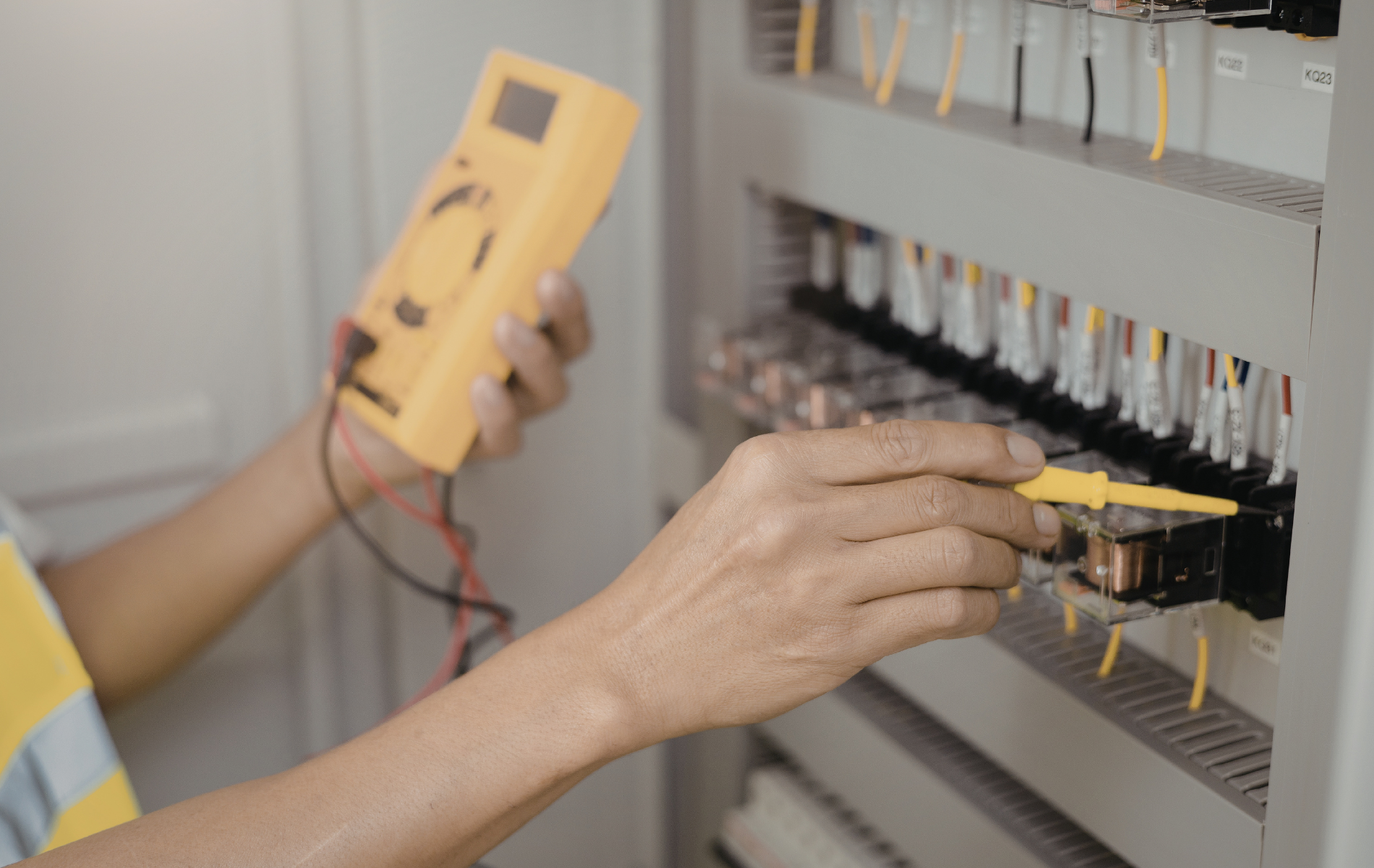 Person using a multimeter to test electrical wiring in a panel.
