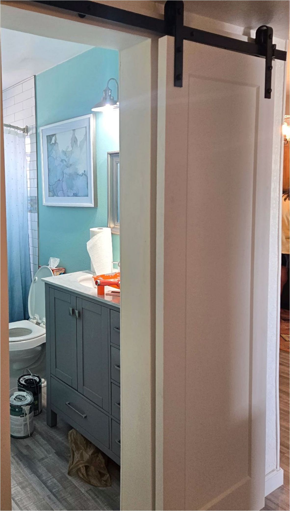 White barn door partially open to reveal a bathroom with blue walls, a gray vanity, and a toilet.