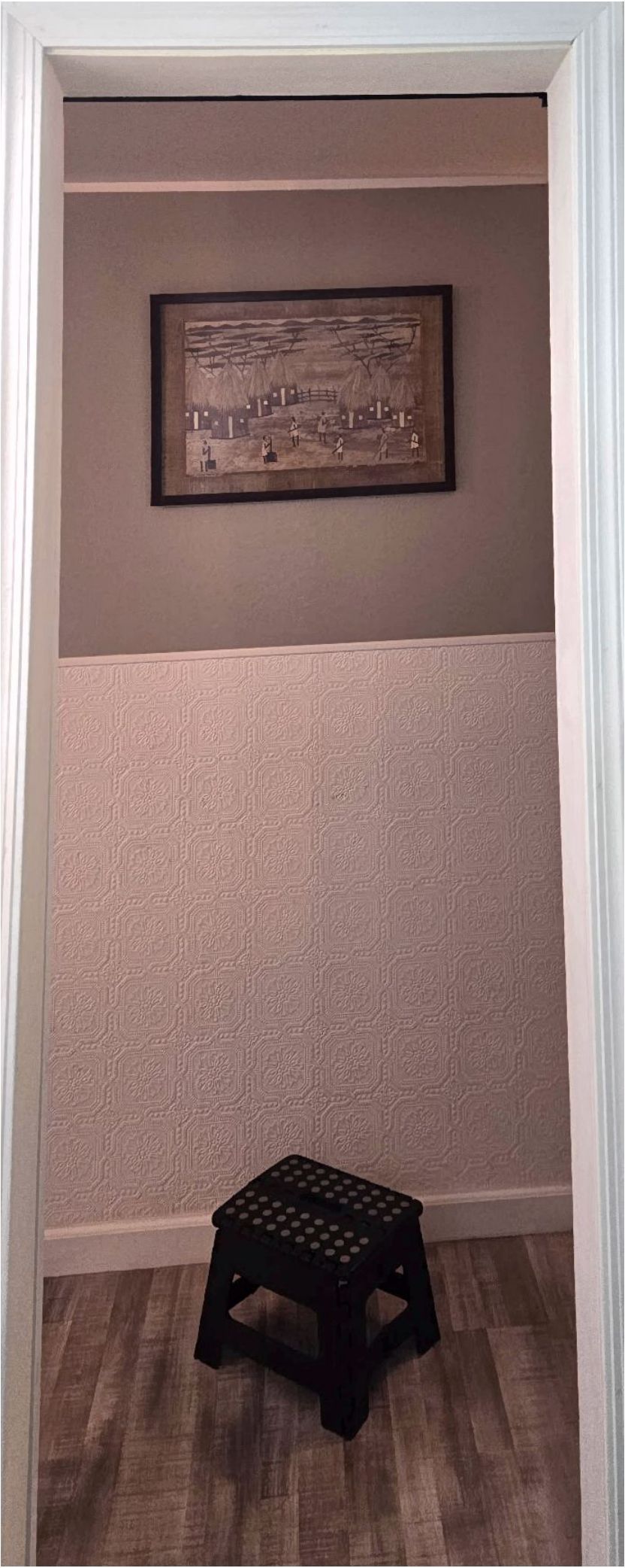 View of a room through a doorway, with a step stool. A framed picture hangs on the wall.