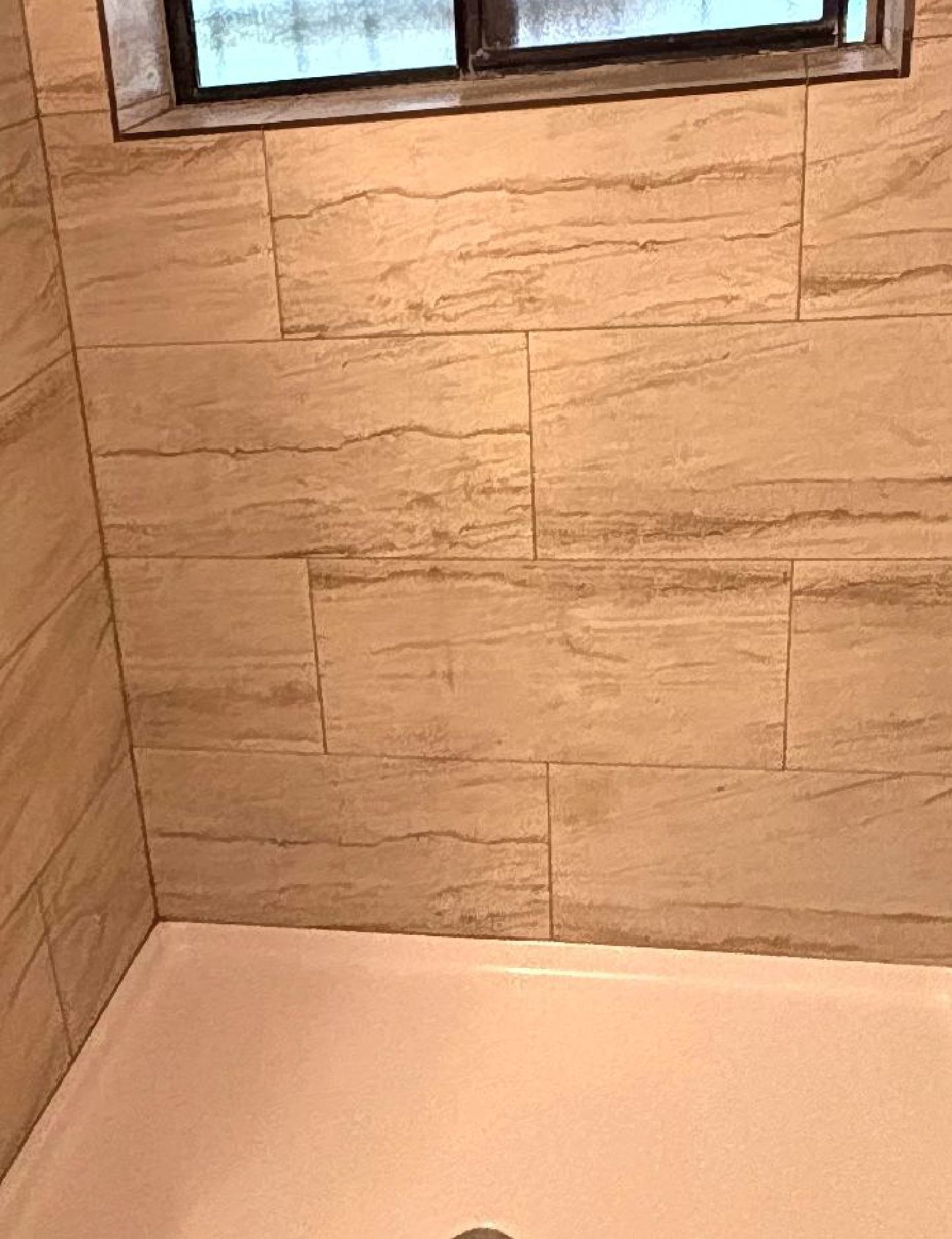 Shower stall with beige tiled walls and white base, small window above.