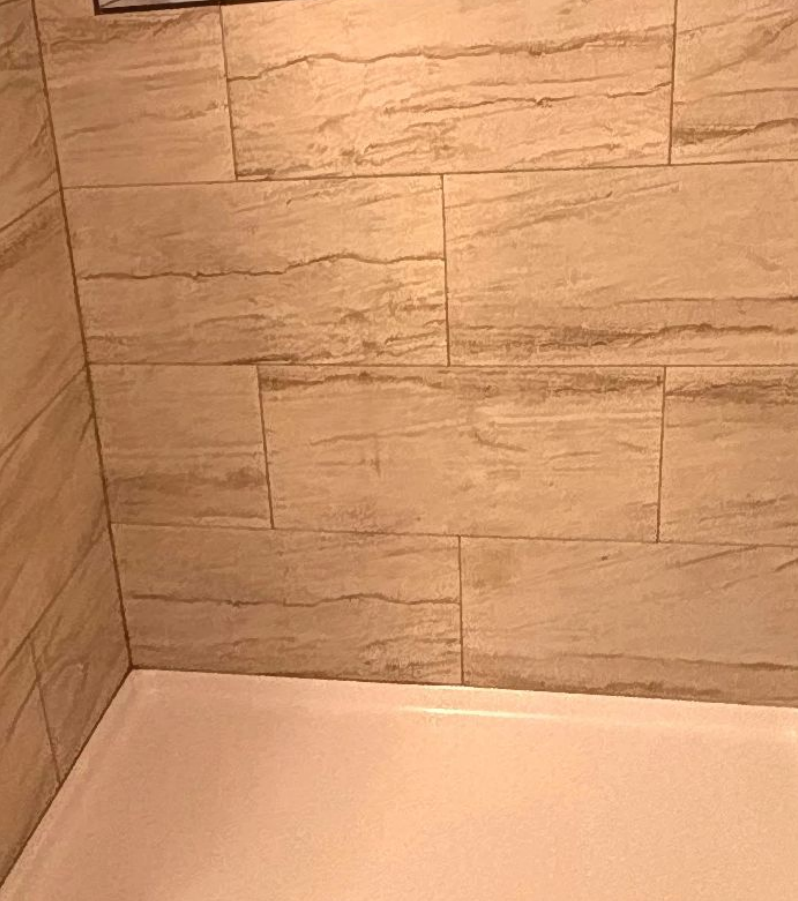 Beige tile shower walls with a white tub.