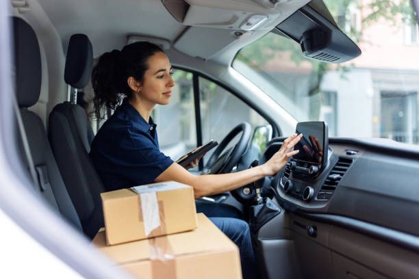 A woman is sitting in the driver's seat of a van holding a tablet.