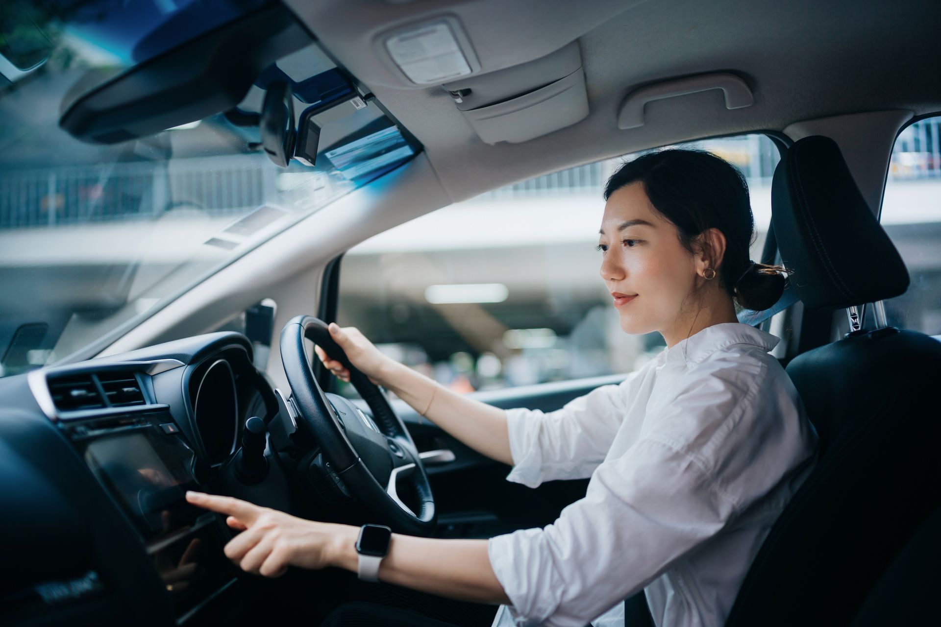 A woman is driving a car and pointing at the dashboard.