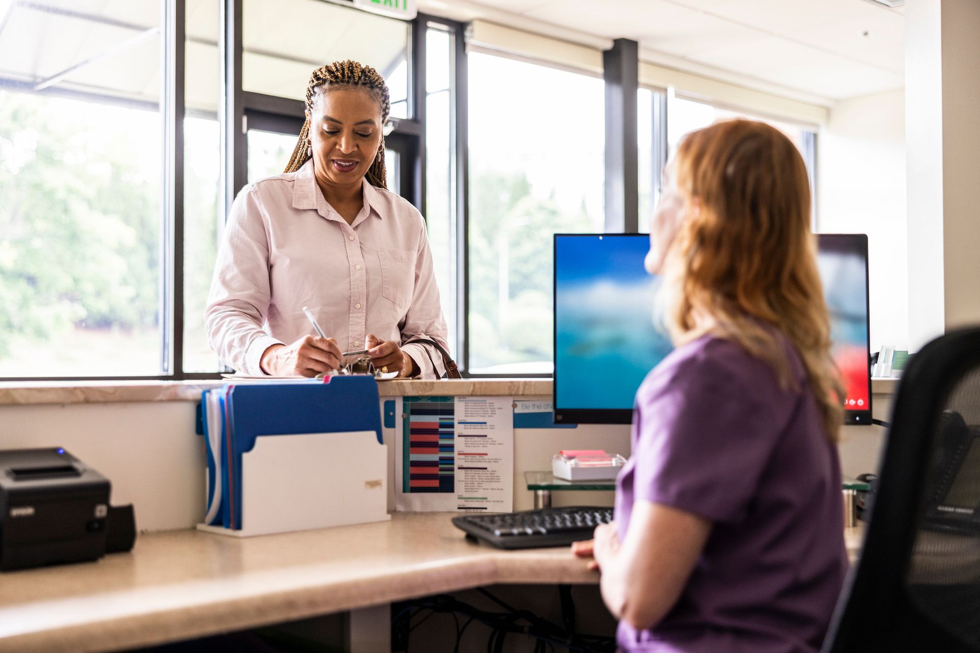 A nurse is talking to a patient at a desk in a hospital.