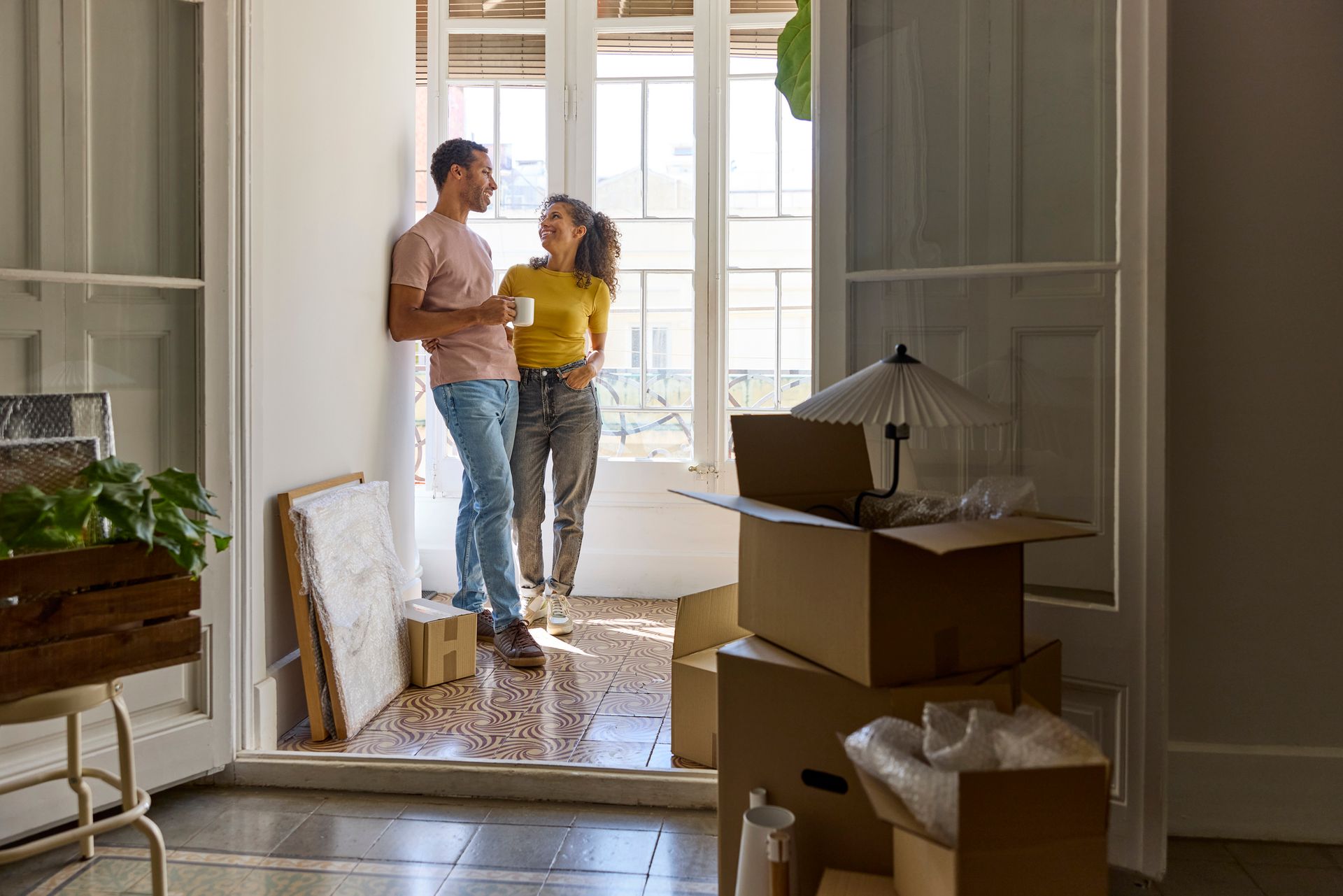 A man and a woman are standing in a living room surrounded by cardboard boxes.