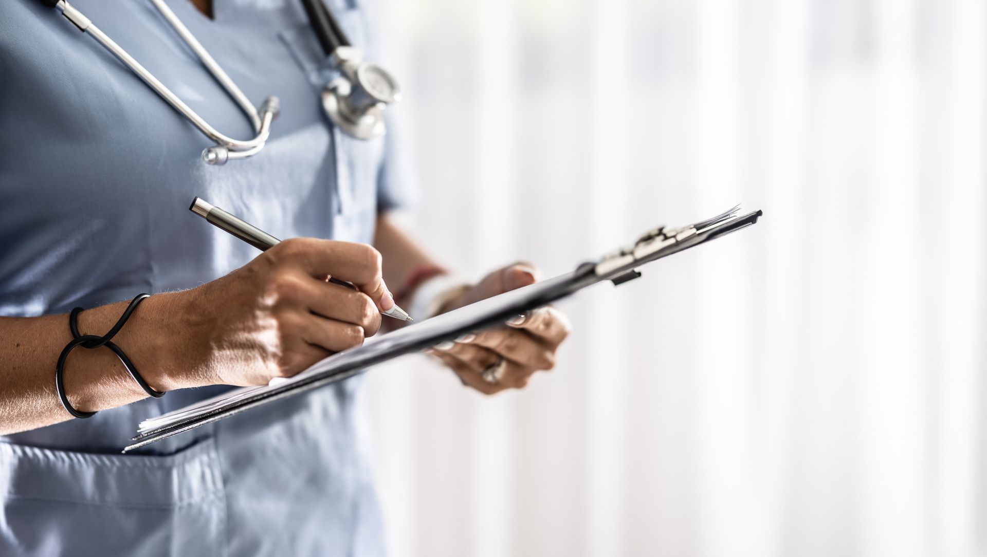 A nurse is writing on a clipboard with a pen.