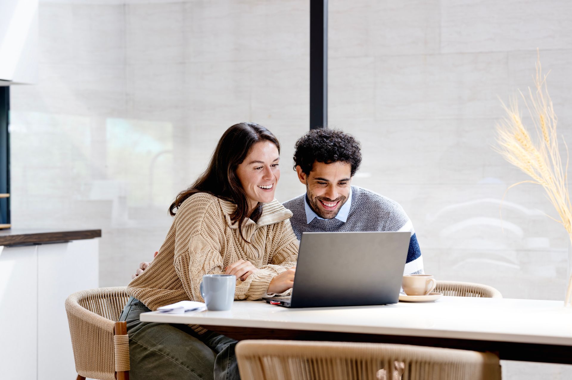 A man and a woman are sitting at a table looking at a laptop computer.