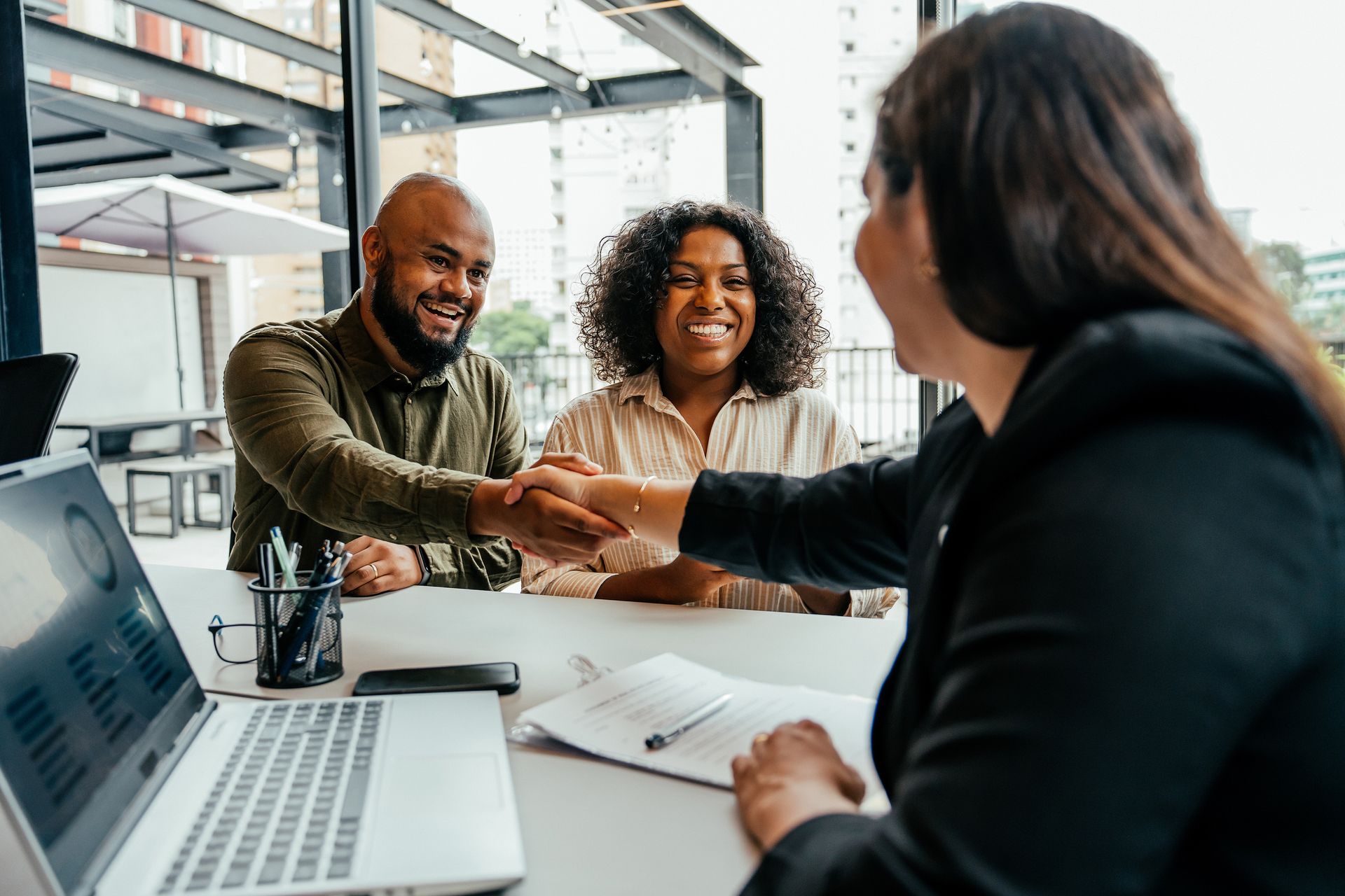 A man and woman are shaking hands with a woman while sitting at a table.