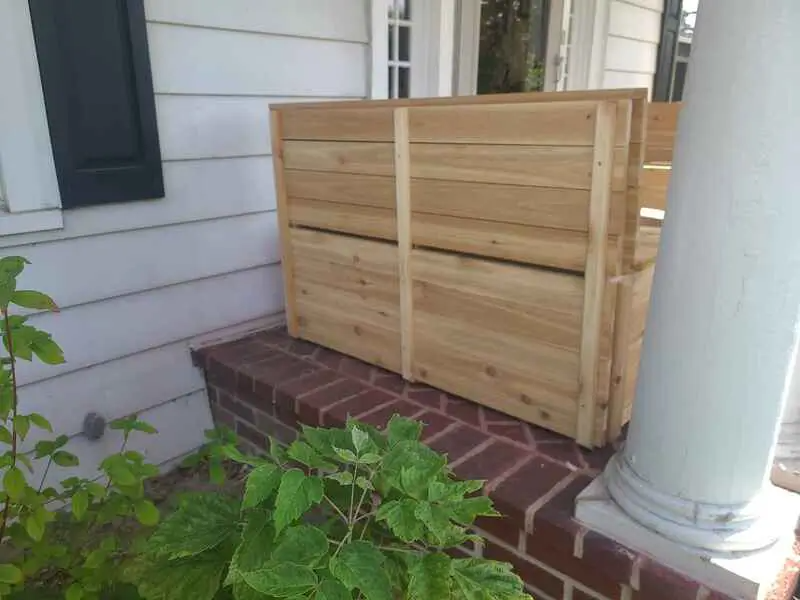 A wooden box is sitting on a porch next to a brick wall.
