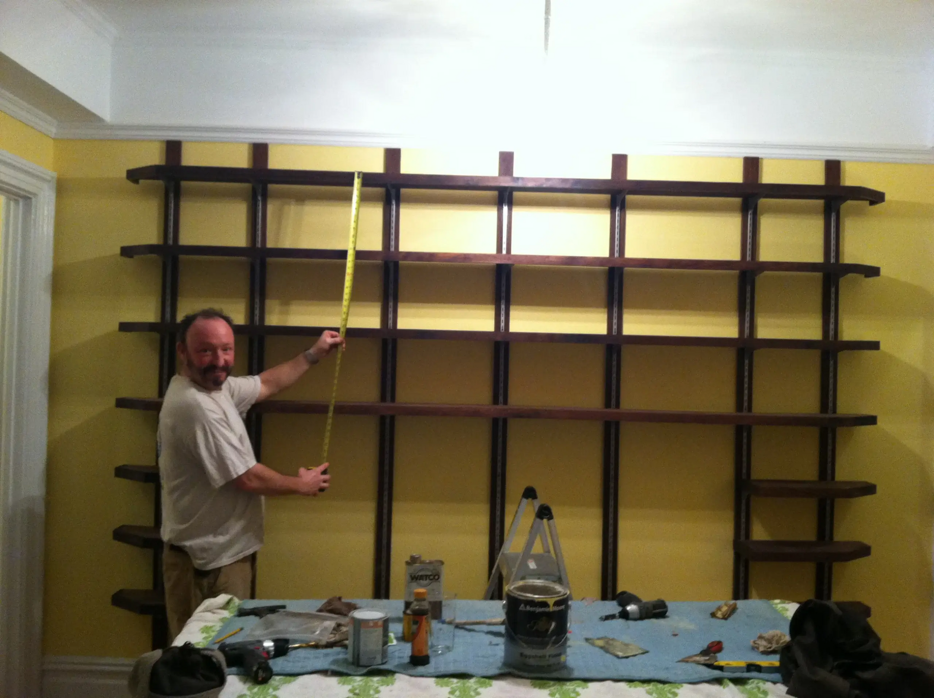 A man is measuring a wall of shelves with a tape measure