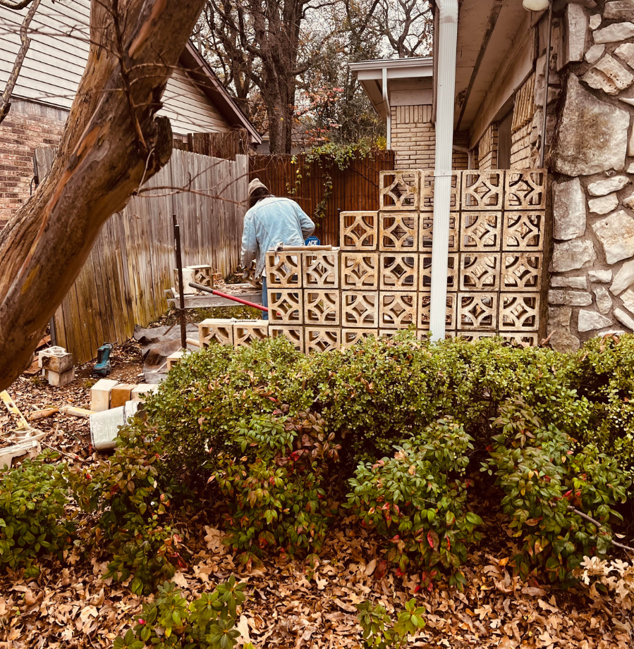 A man is working on a fence with bricks in front of a house