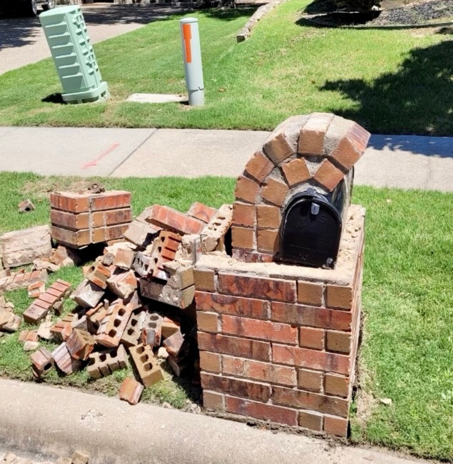 A brick mailbox sits in the grass next to a pile of bricks