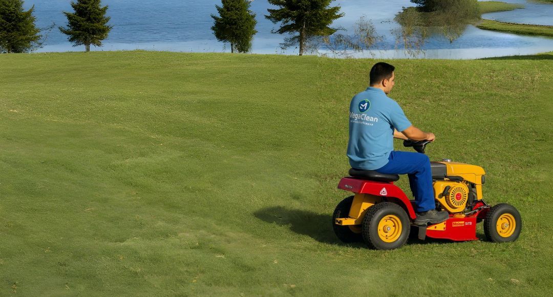 Hombre en un cortacésped rojo y amarillo cortando hierba en un campo verde junto a un lago.