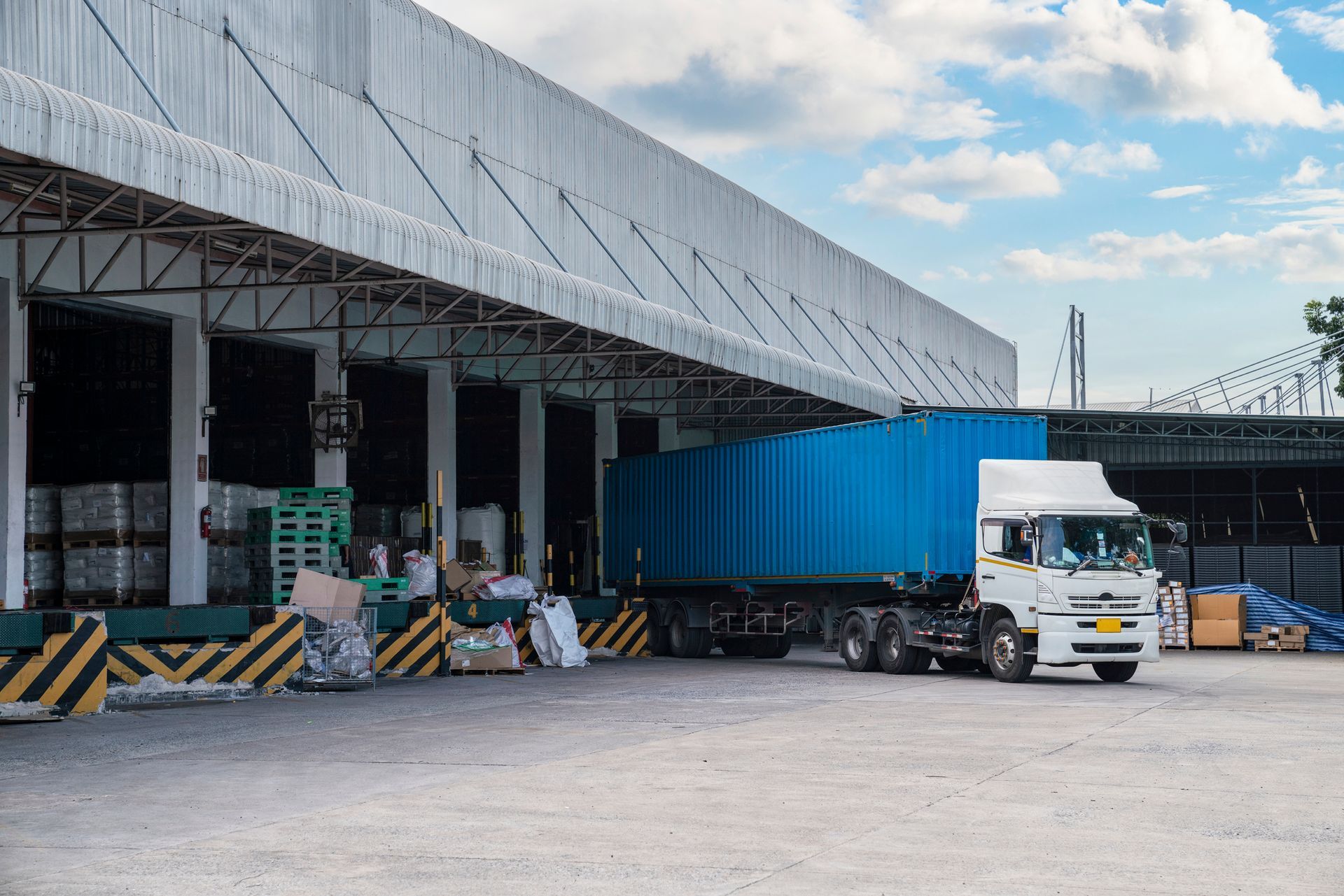 Truck backing into a loading dock with a blue container. Sunny day, exterior shot of a warehouse.
