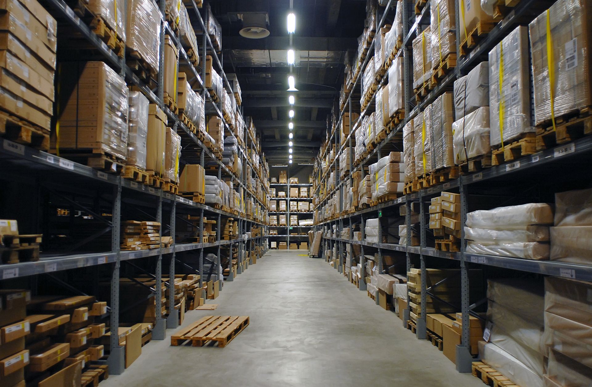 Warehouse interior with rows of shelves filled with boxes. Empty pallet on the floor.