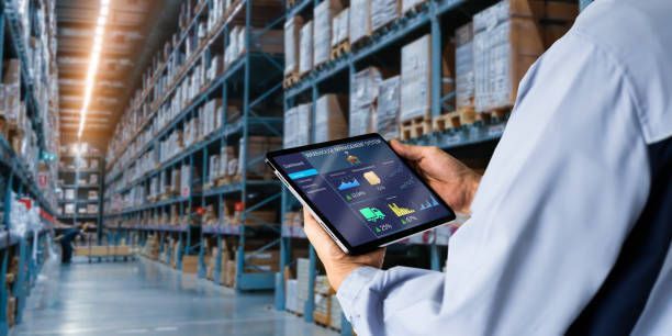 Warehouse worker using tablet to manage inventory. Shelves of boxes fill the background.