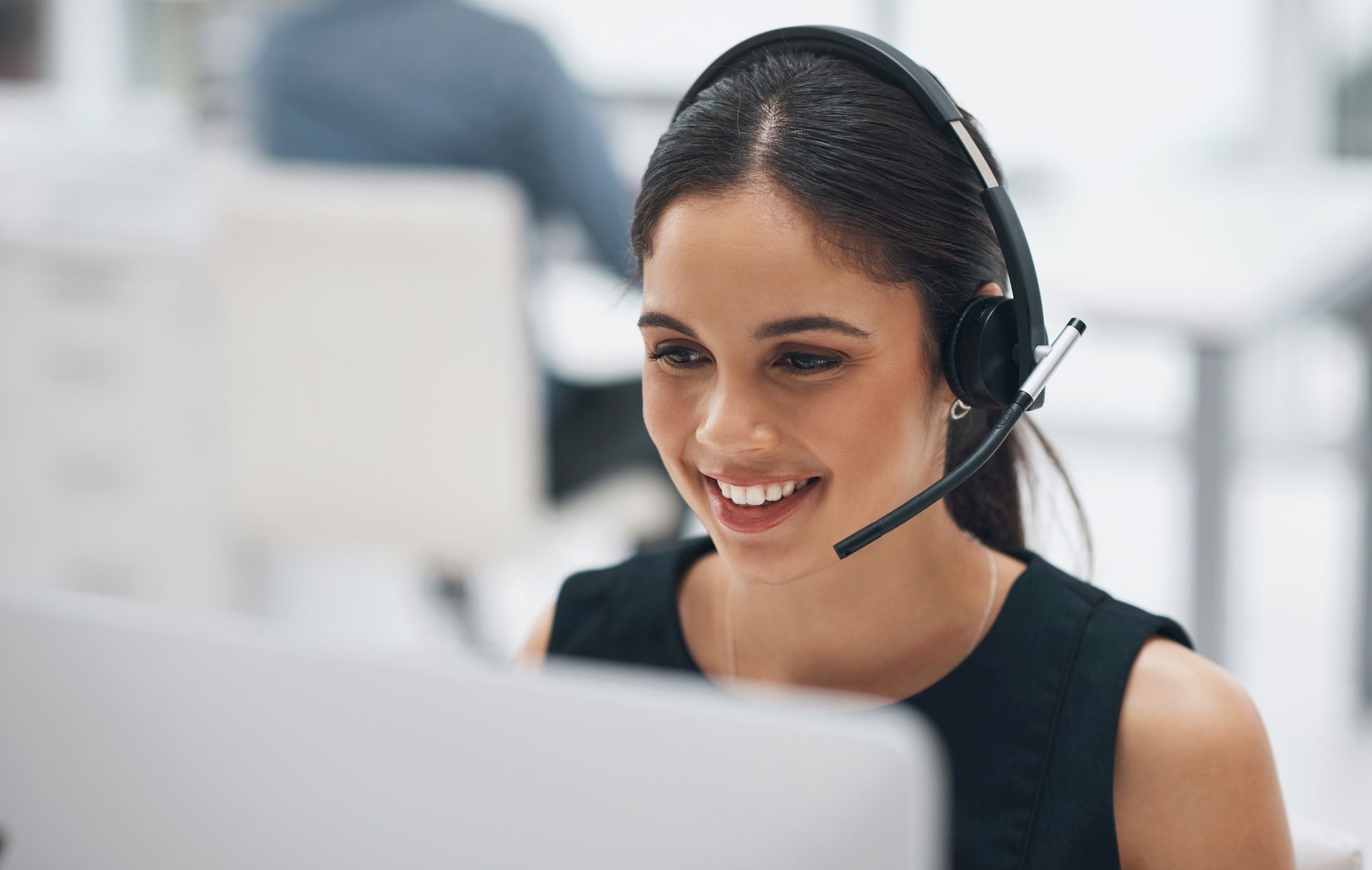 Woman wearing headset, smiling, working on computer in office.