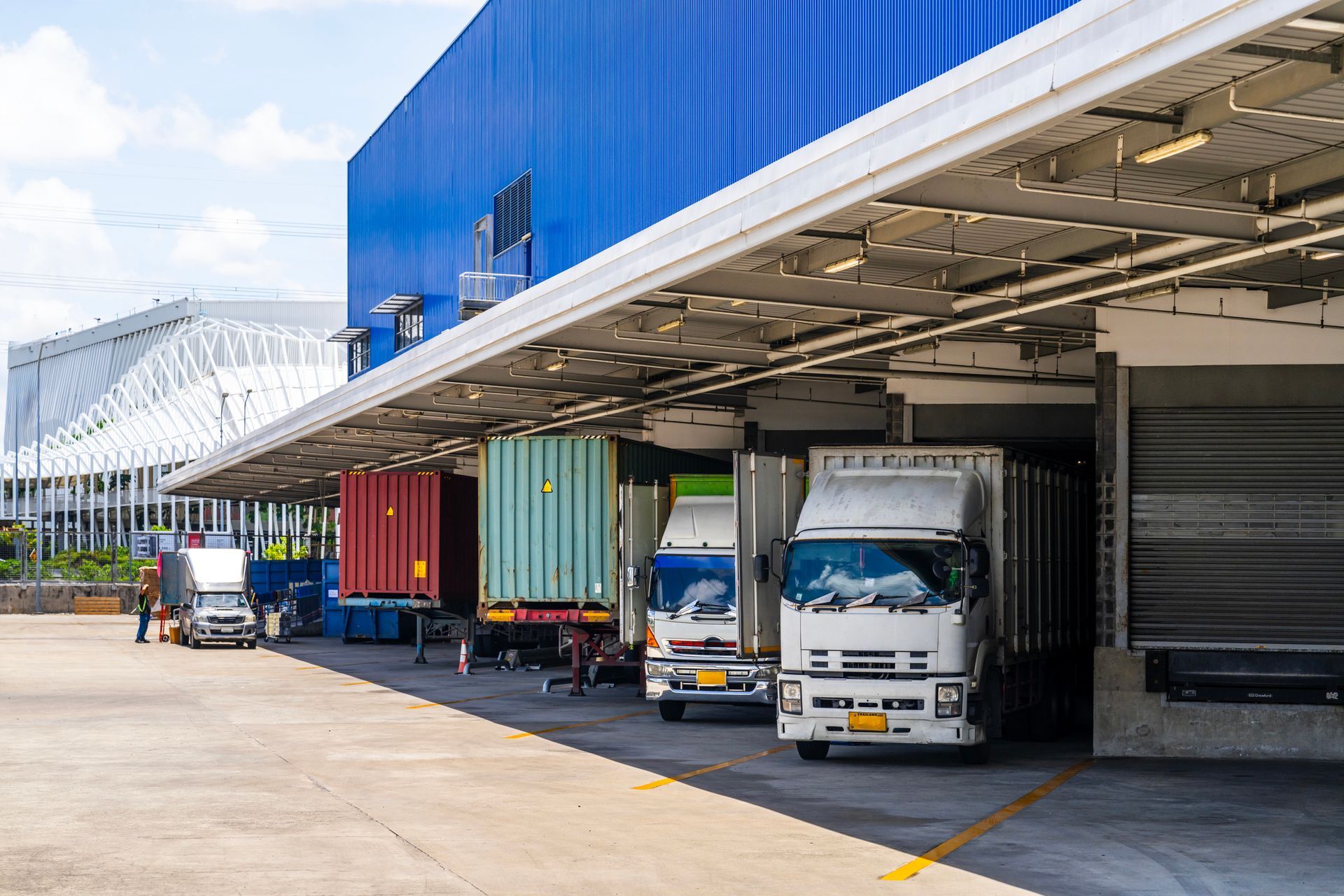 Trucks loading at a warehouse dock. Blue building with covered loading bays, trucks parked, clear day. Trucks loading at a warehouse dock. Blue building with covered loading bays, trucks parked, clear day.