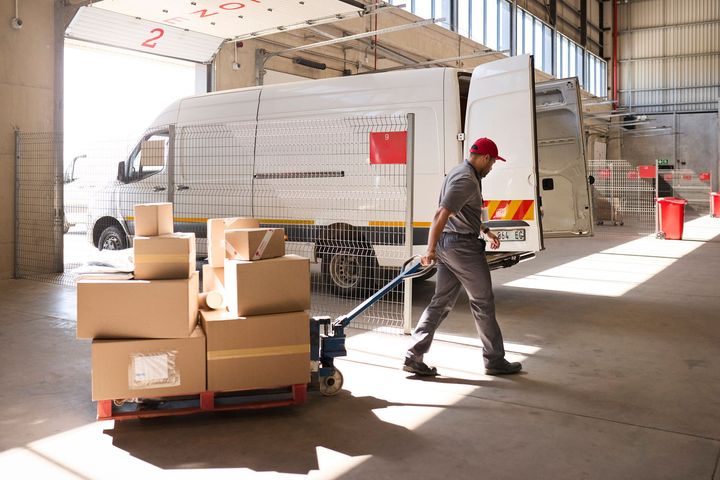 Delivery person pulls a pallet of boxes from a cargo van inside a warehouse.