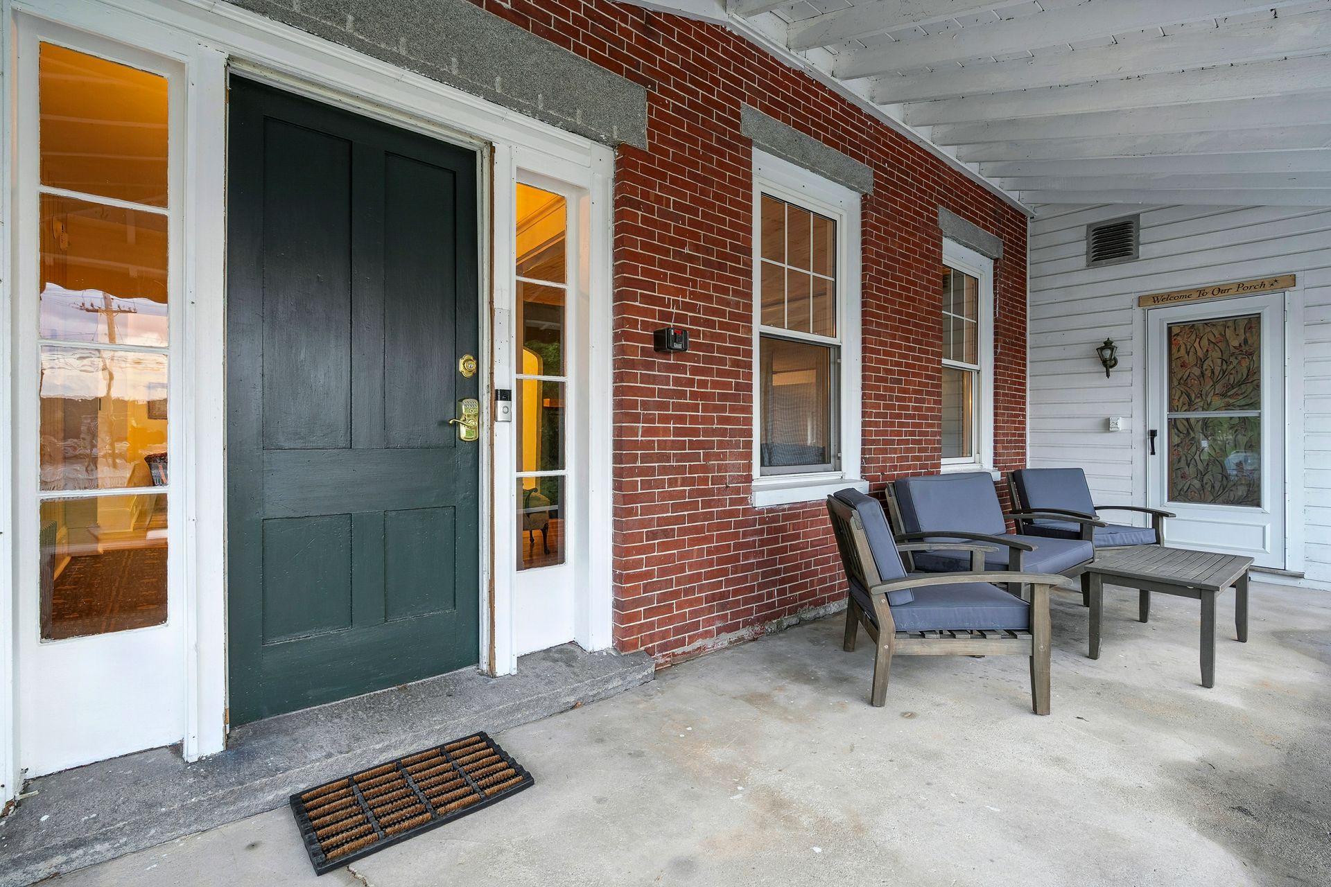 Exterior porch with dark green door, brick wall, and gray seating.
