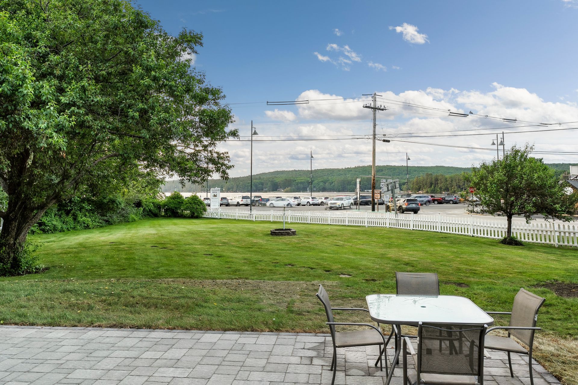 Lawn with a table and chairs, overlooking a harbor with boats and a cloudy sky.